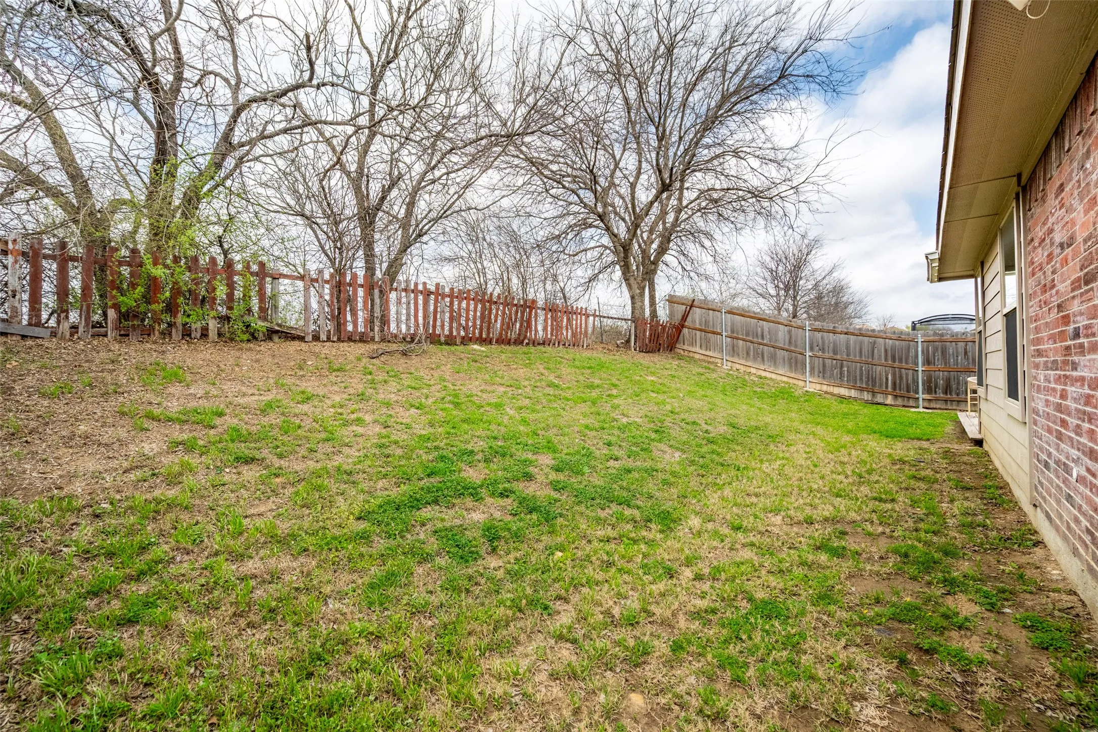 Expansive backyard featuring a partial brick exterior, wood privacy fencing, and mature trees