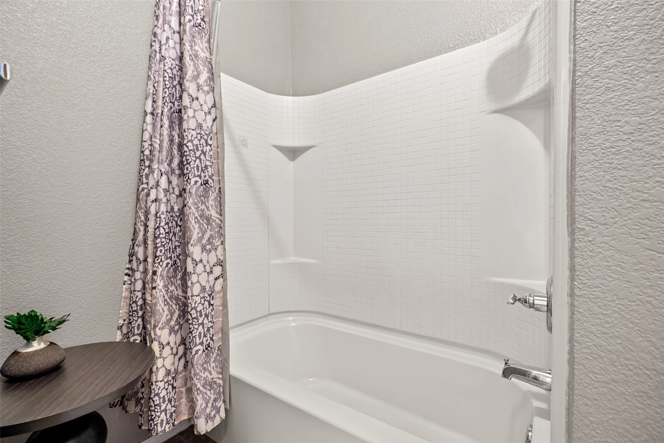 Bathtub with integrated shower surround featuring textured wall panels and built-in shelving