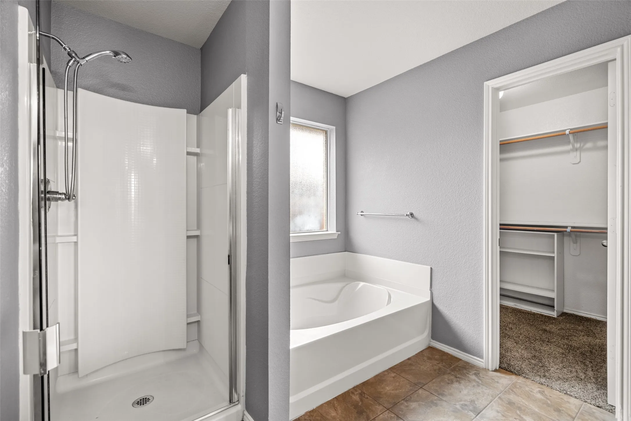 Walk-in shower with curved white paneling, garden tub, window with frosted glass, and a closet with built-in shelving