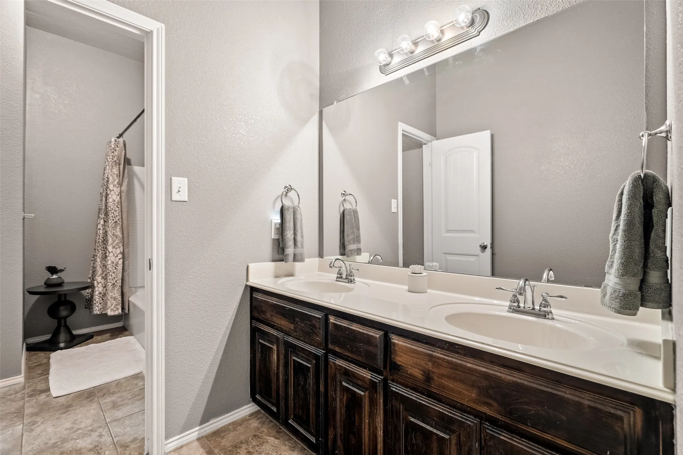 Double vanity with white oval sinks, dark wood-finish cabinetry, and a full-width mirror