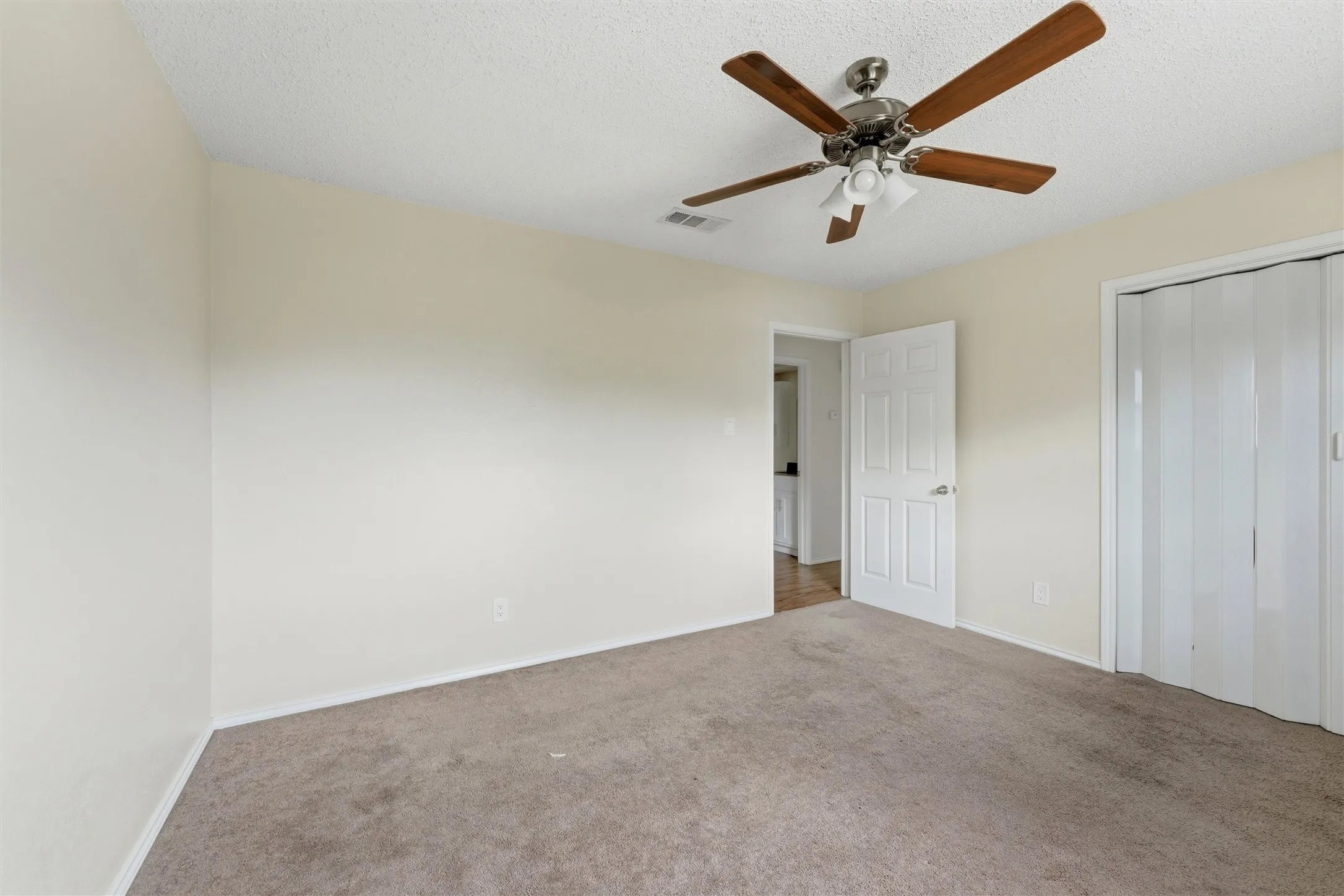 Neutral-toned walls, carpeted flooring, ceiling fan with integrated lighting, paneled door, and bi-fold closet doors
