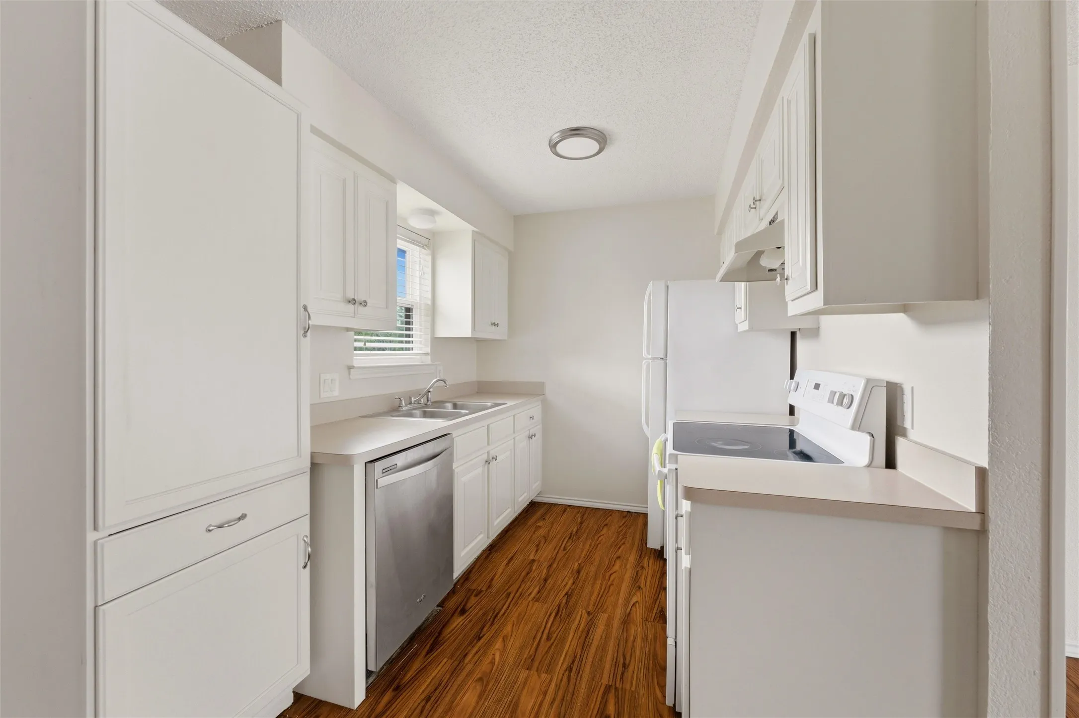 Kitchen featuring white cabinetry, wood-finish flooring, a stainless steel dishwasher, and a double basin sink