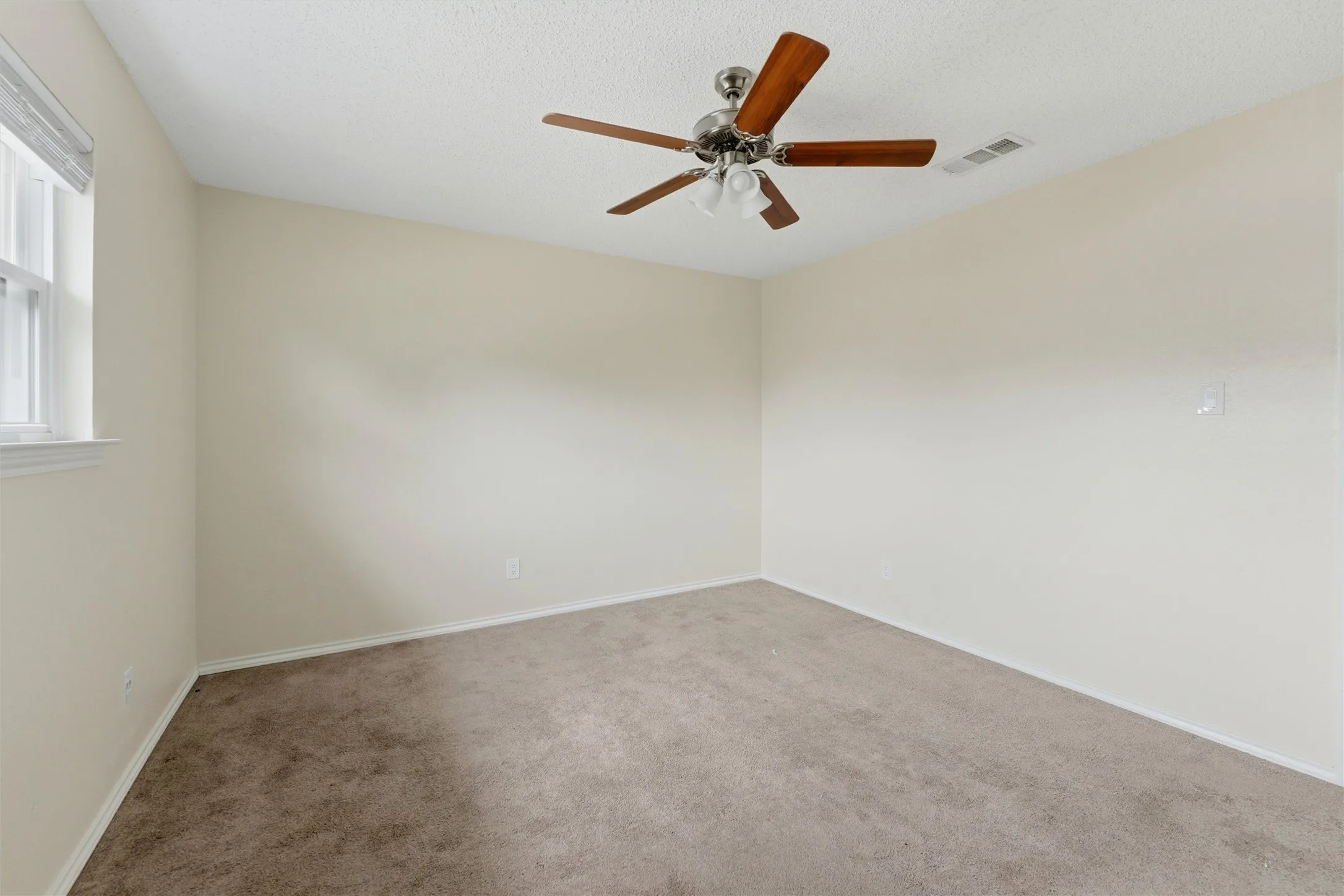 Carpeted flooring, neutral wall tones, ceiling fan with wood-finish blades, and window with blinds