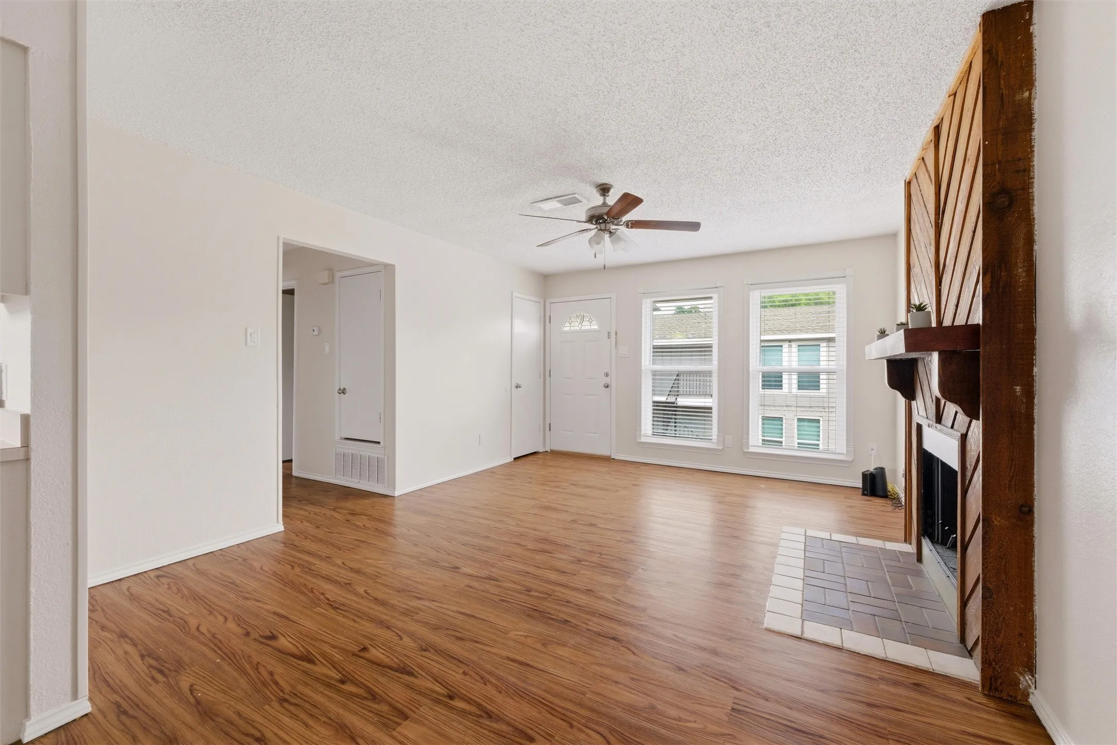 Spacious living area featuring wood-finish flooring, a ceiling fan, and multiple windows