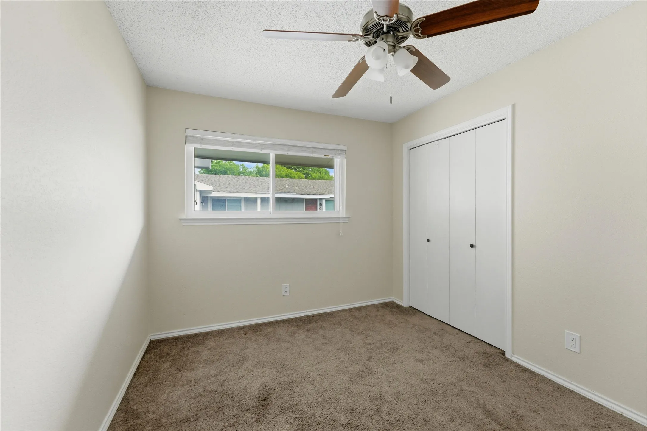 Carpeted room featuring a ceiling fan with light fixture, a window with white trim, and a bi-fold closet