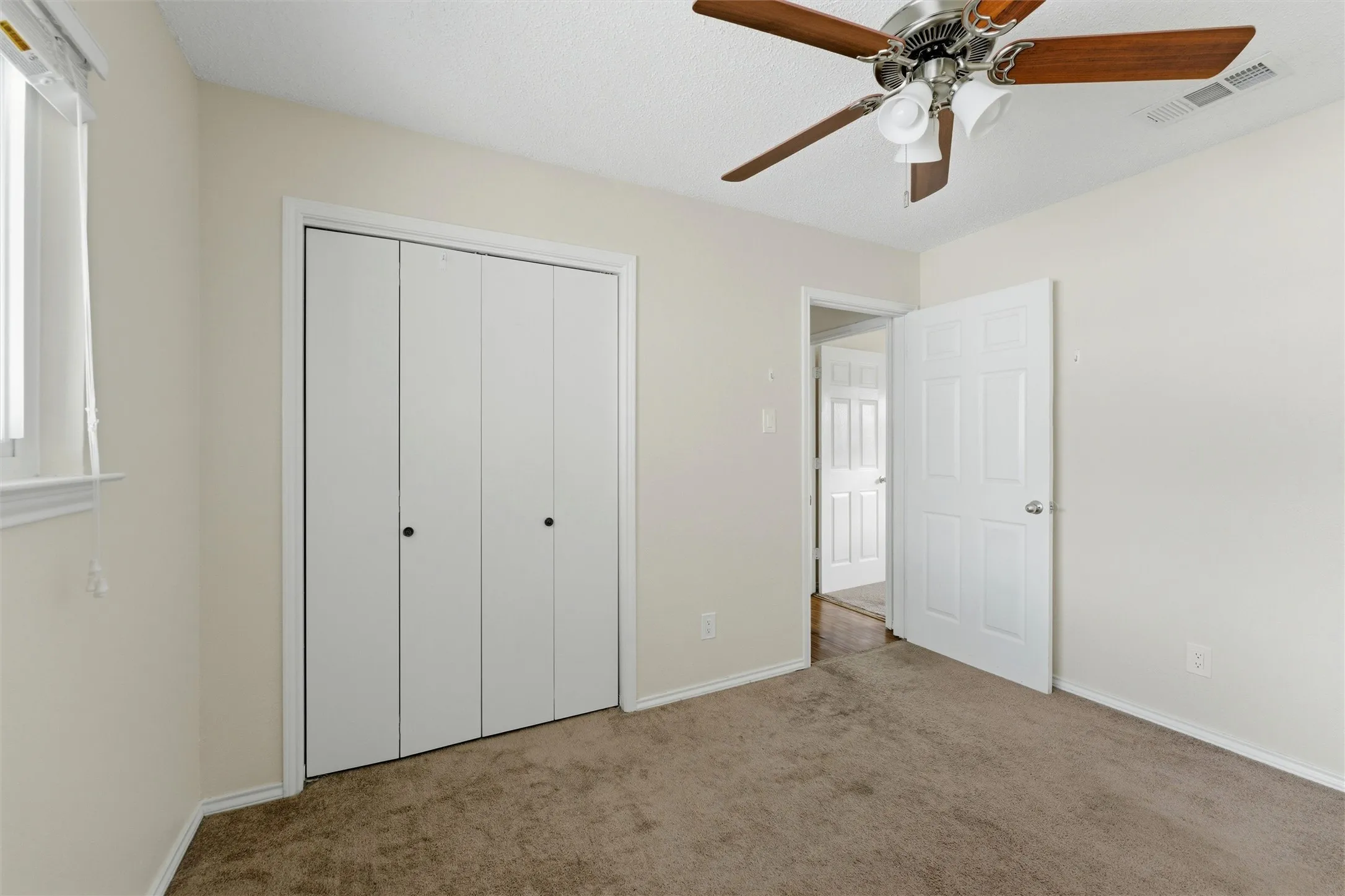 Bi-fold closet doors, ceiling fan with integrated lighting, window with blinds, and neutral carpeting
