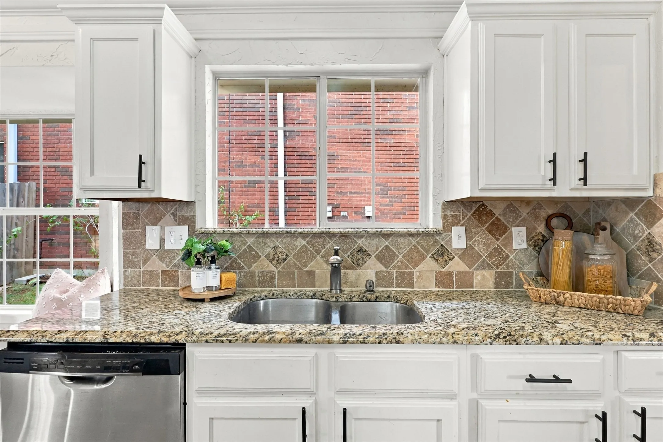 White shaker-style cabinetry with black hardware, granite countertops, stainless steel undermount sink, and a tiled backsplash