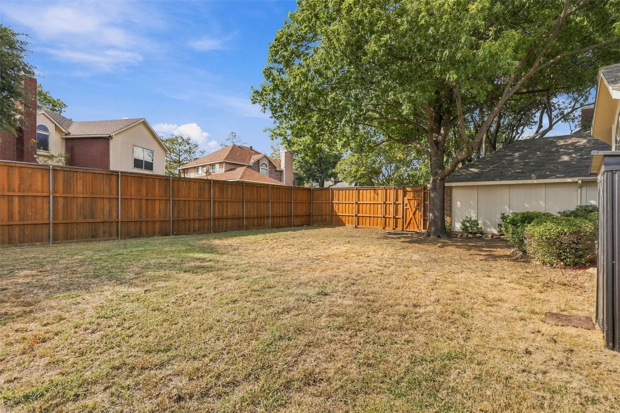 Expansive backyard featuring a wood privacy fence, mature trees, and a detached structure