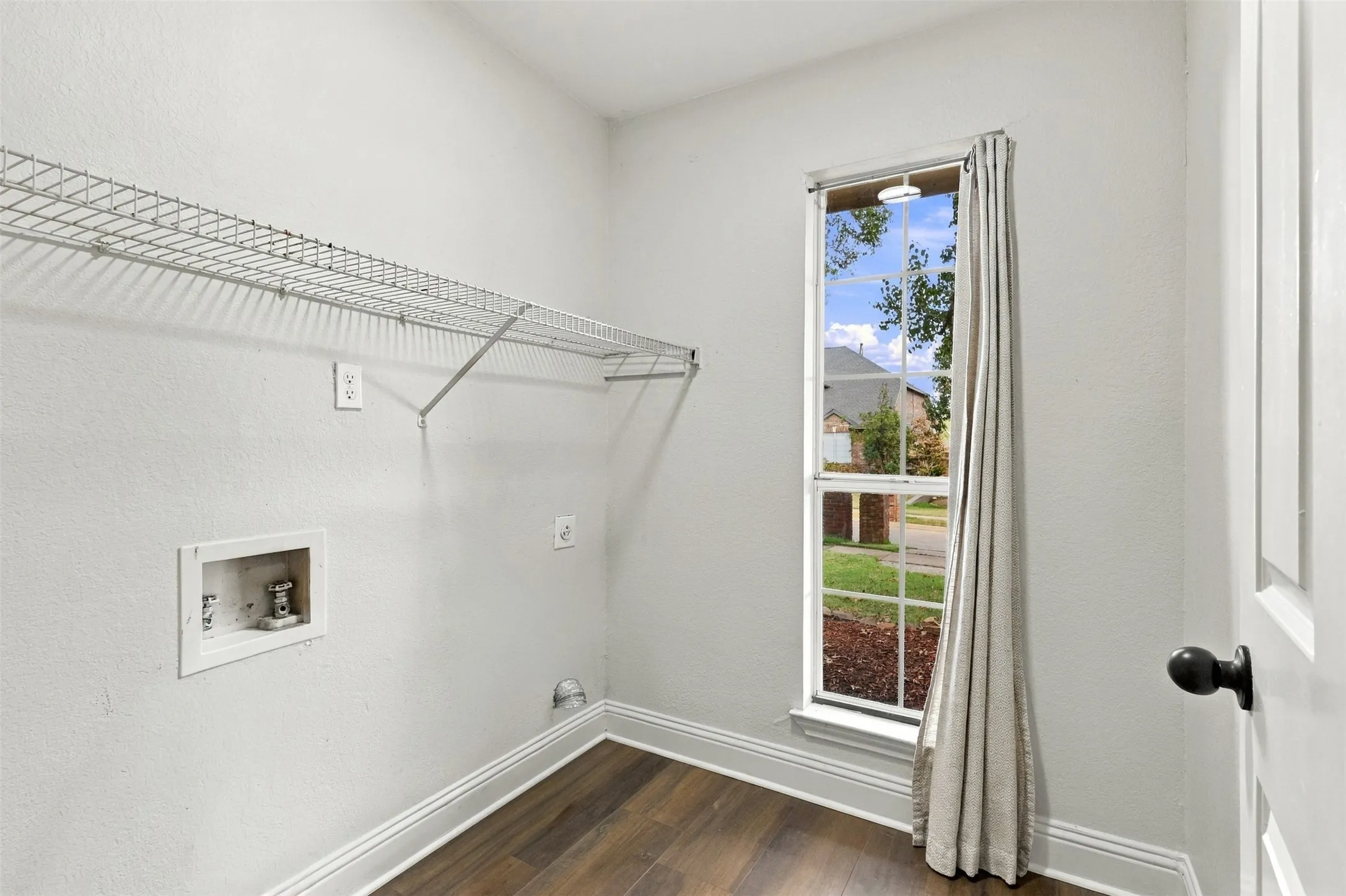 Wood-finish flooring, single window, white walls, and wire shelving