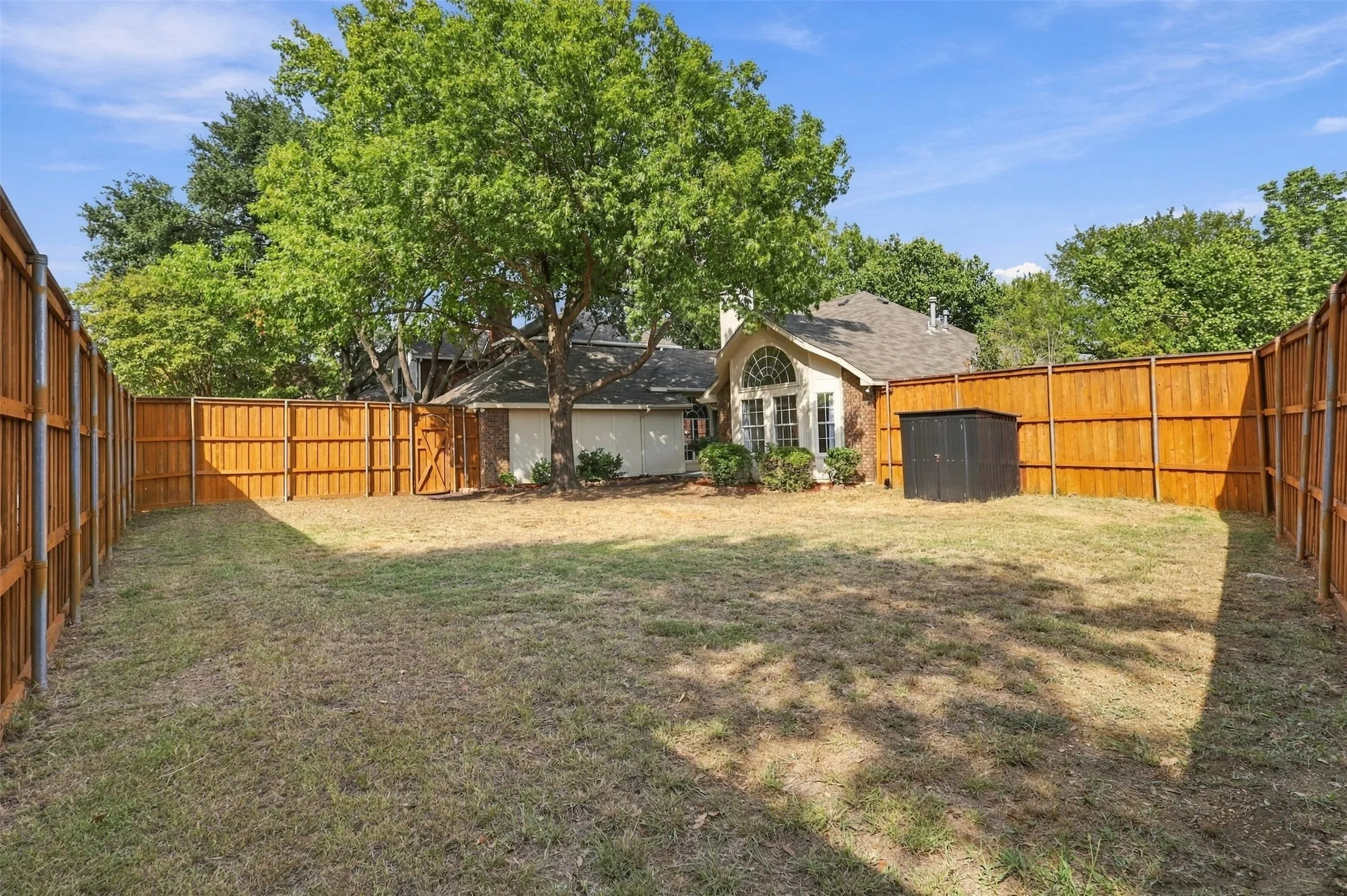 Fenced backyard with a privacy fence, mature trees, and a storage shed