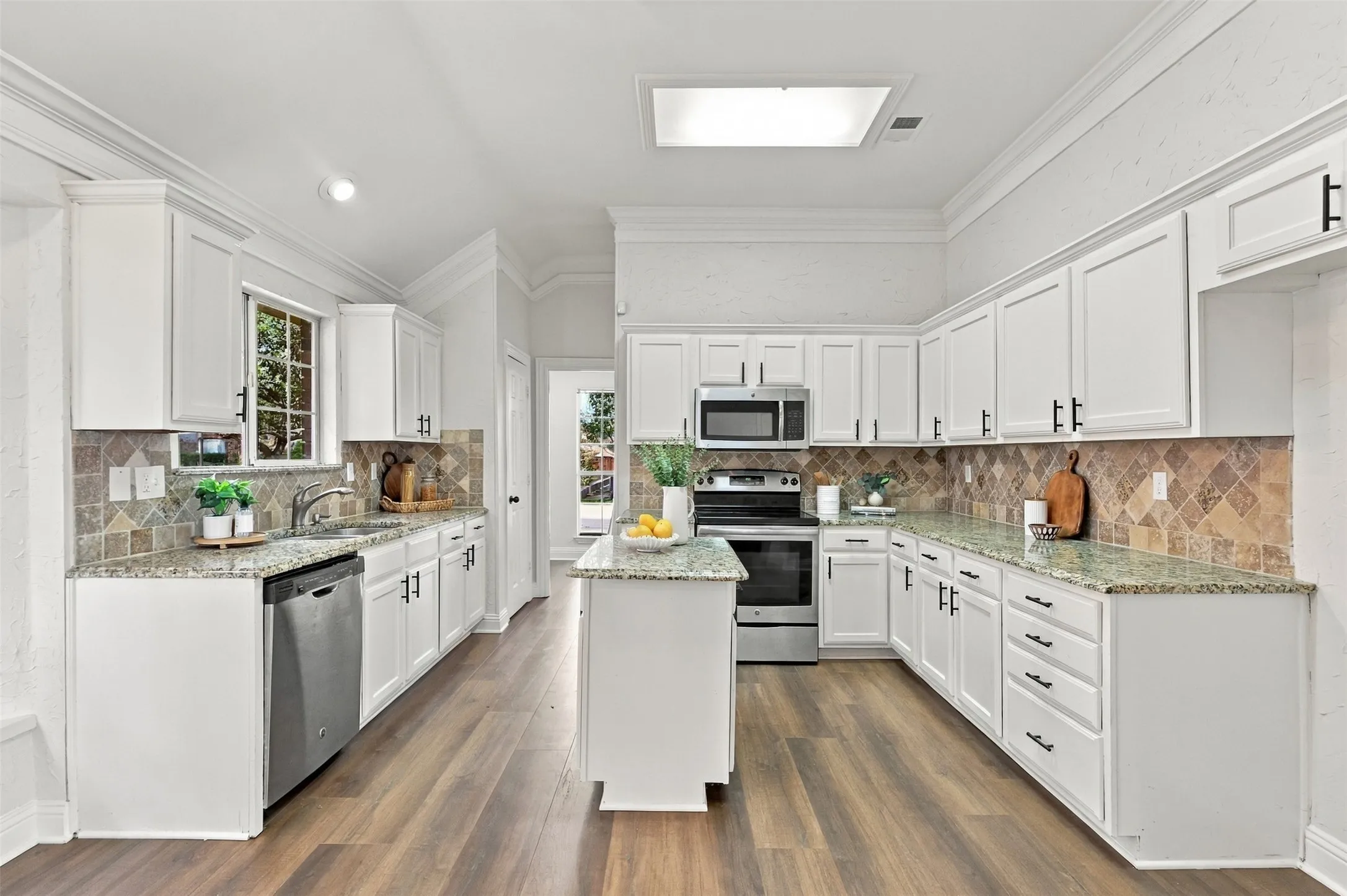 White cabinetry with black hardware, wood-finish flooring, granite countertops, tile backsplash, and stainless steel appliances