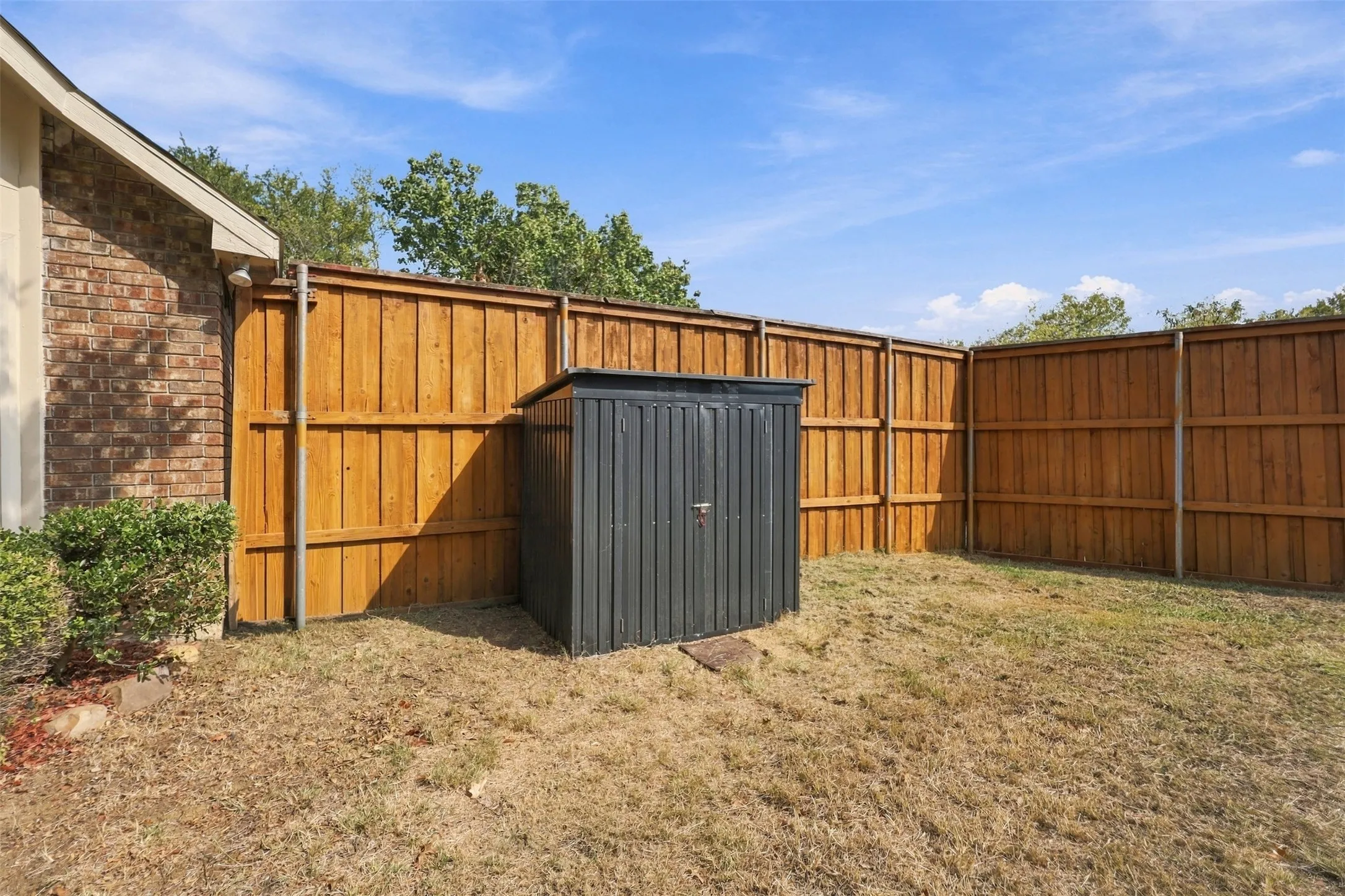 Wood-paneled fencing enclosing the property, featuring a built-in storage shed and brick exterior siding