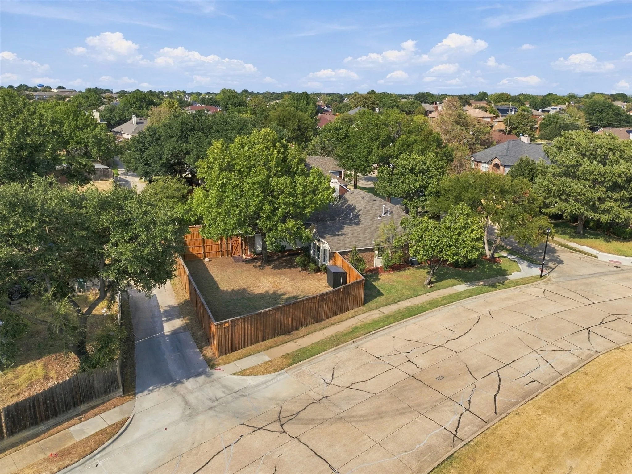 Fenced backyard with mature trees and a paved driveway
