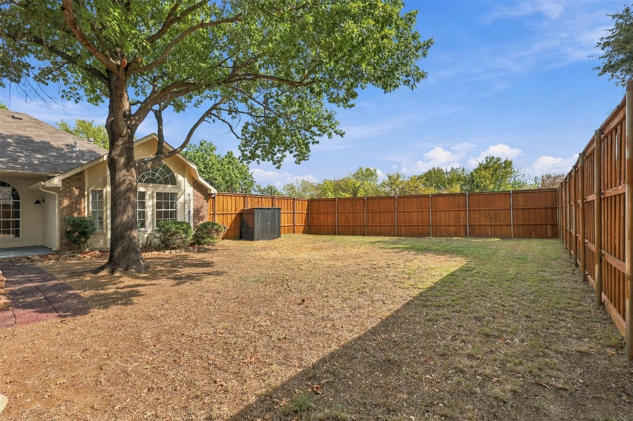 Expansive backyard featuring a full privacy fence, mature trees, and a storage shed