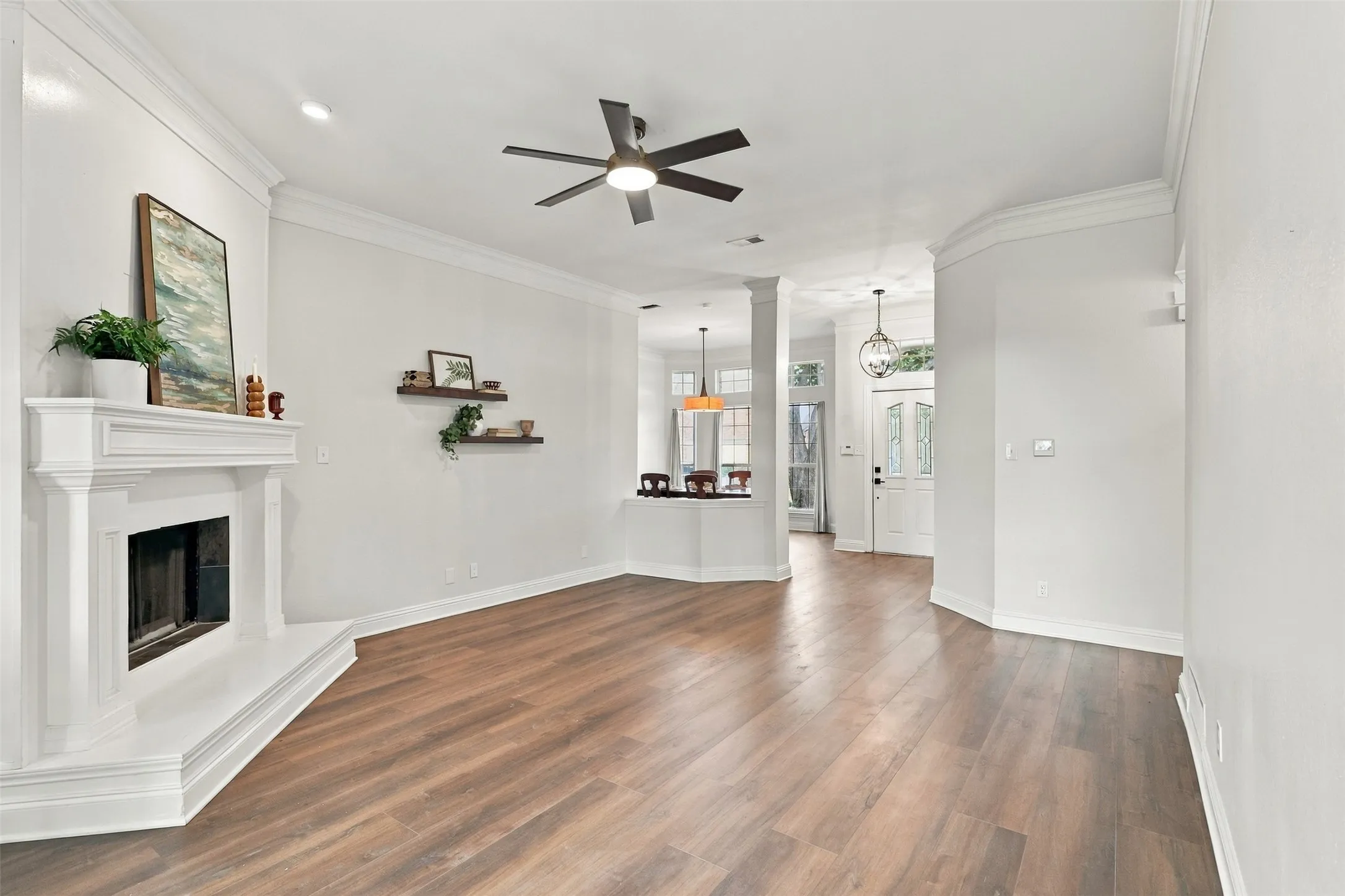 Living area featuring wood-finish flooring, a white mantel fireplace, and crown molding