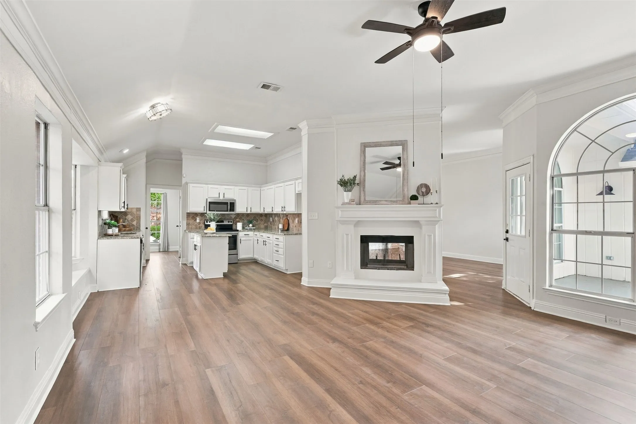 Open-concept layout with wood-finish flooring, white kitchen cabinetry, stainless steel appliances, and a fireplace