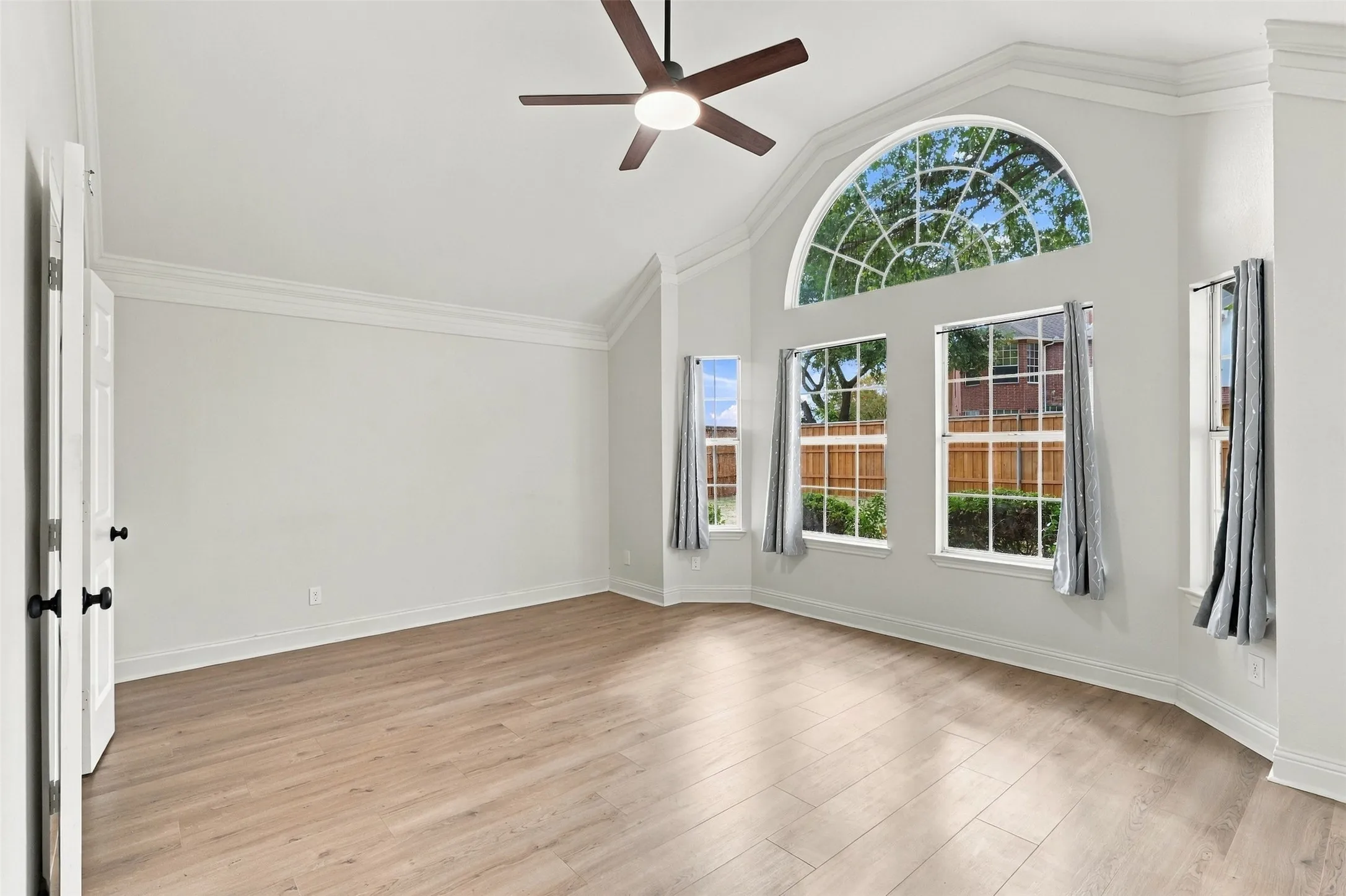 Vaulted ceiling with an arched window, wood-finish flooring, and crown molding