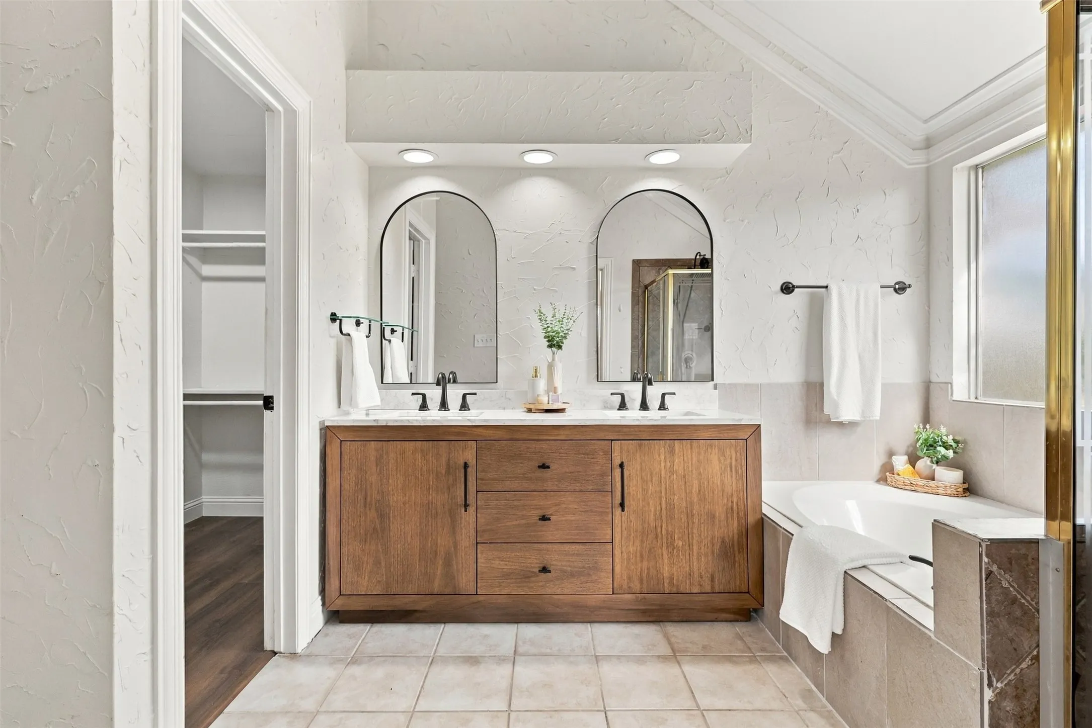 Dual vanity with wood-finish cabinetry and integrated sinks, complemented by arched mirrors and recessed lighting