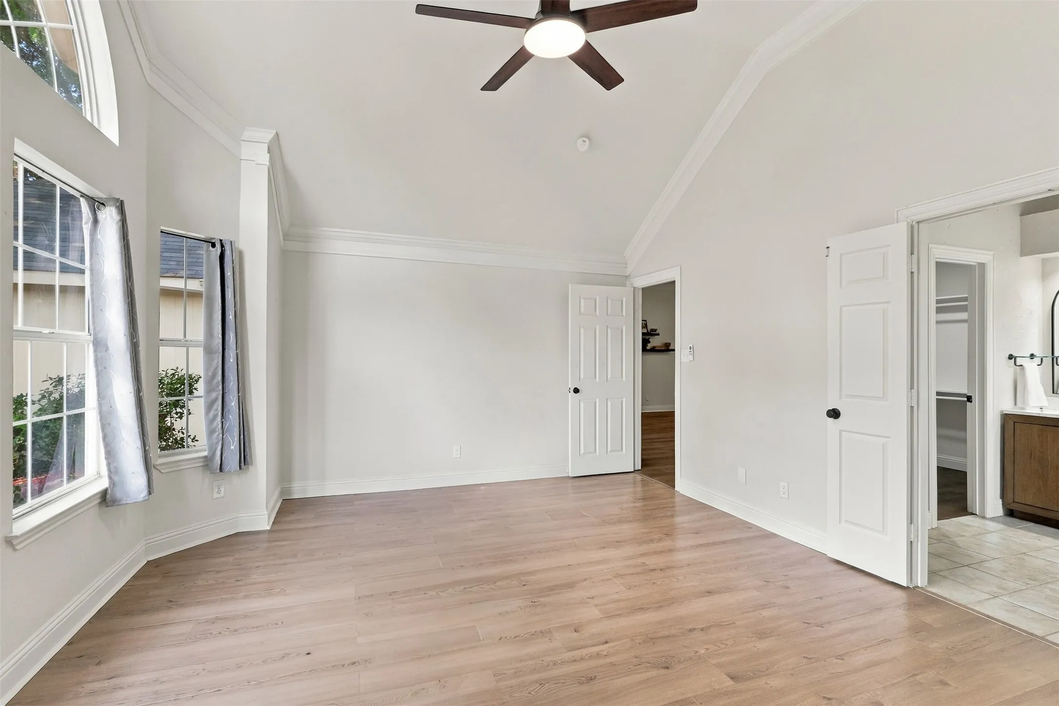 Vaulted ceiling with crown molding, wood-finish flooring, ceiling fan with integrated lighting, multiple windows, and paneled doors