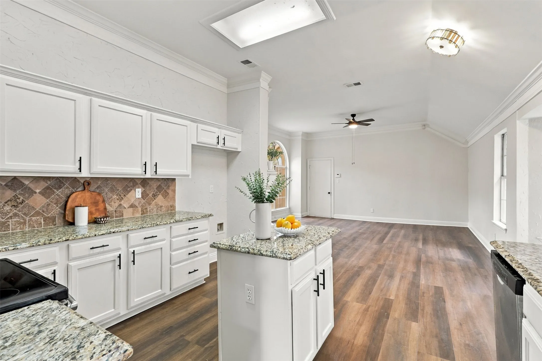 White cabinetry with black hardware, granite countertops, patterned tile backsplash, wood-finish flooring, and vaulted ceilings
