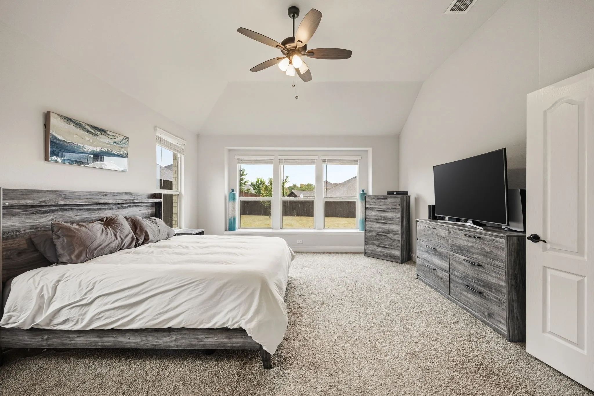 Spacious primary suite with vaulted ceilings and recessed lighting, anchored by a wood-finish platform bed with upholstered headboard