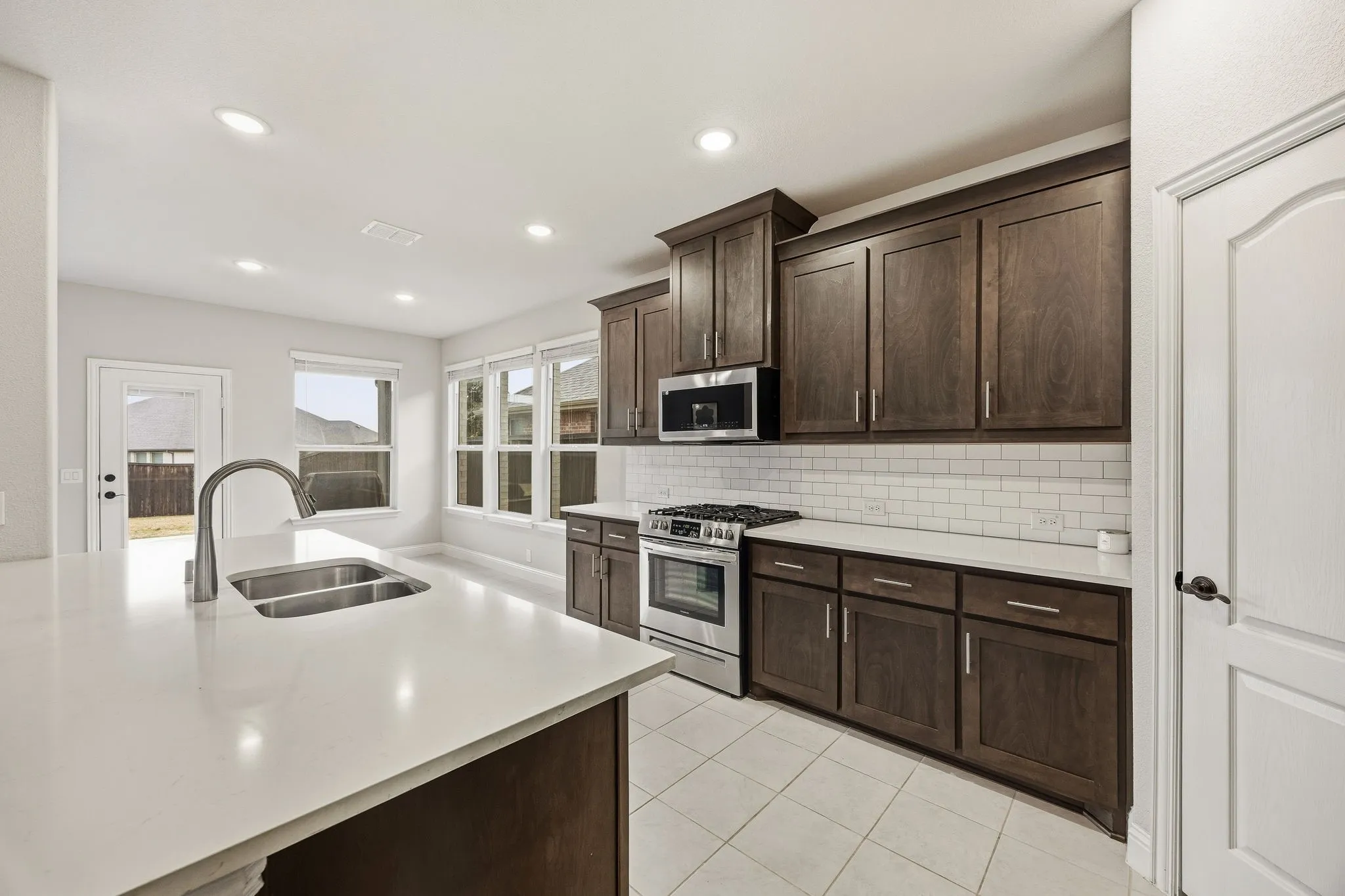 Kitchen featuring a large island with an undermount double basin sink and gooseneck faucet, dark wood-finish cabinetry, white subway tile backsplash, stainless steel appliances, and tile flooring
