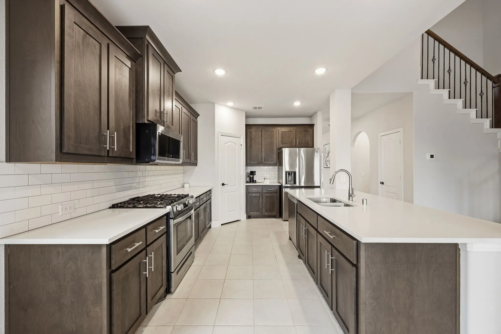 Kitchen featuring dark wood cabinetry, white subway tile backsplash, light countertops, stainless steel appliances, and a central island with an integrated sink