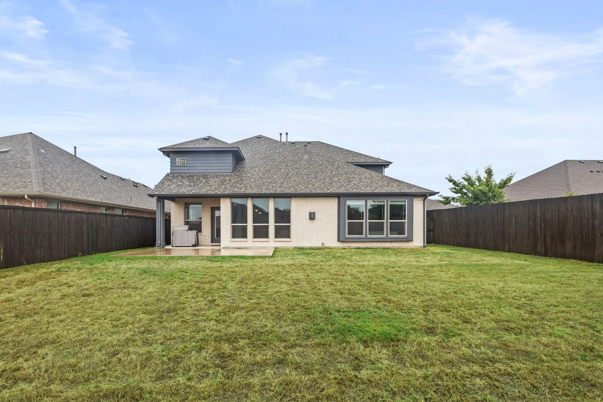 Expansive grassy yard with wood fencing, a covered patio, and multi-pane windows