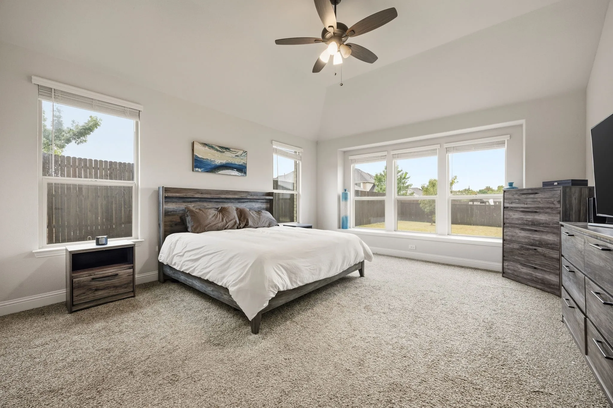 Vaulted ceiling with ceiling fan, expansive window wall, three individual windows, light neutral wall color, and carpeted flooring