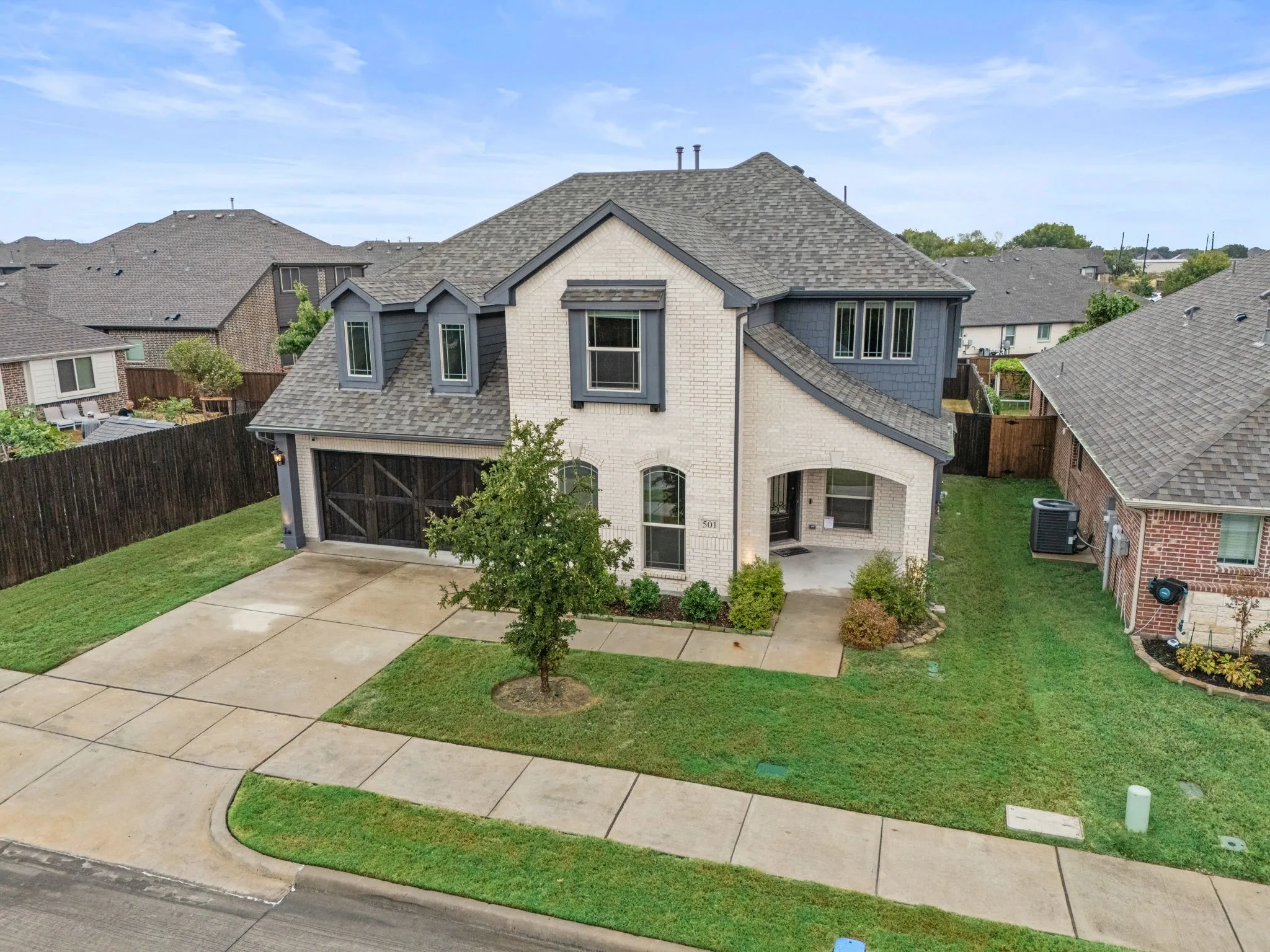 Two-story residence featuring a gray asphalt shingle roof, white brick facade, dark gray siding accents, an attached garage with a dark wood-finish door, and a covered entry
