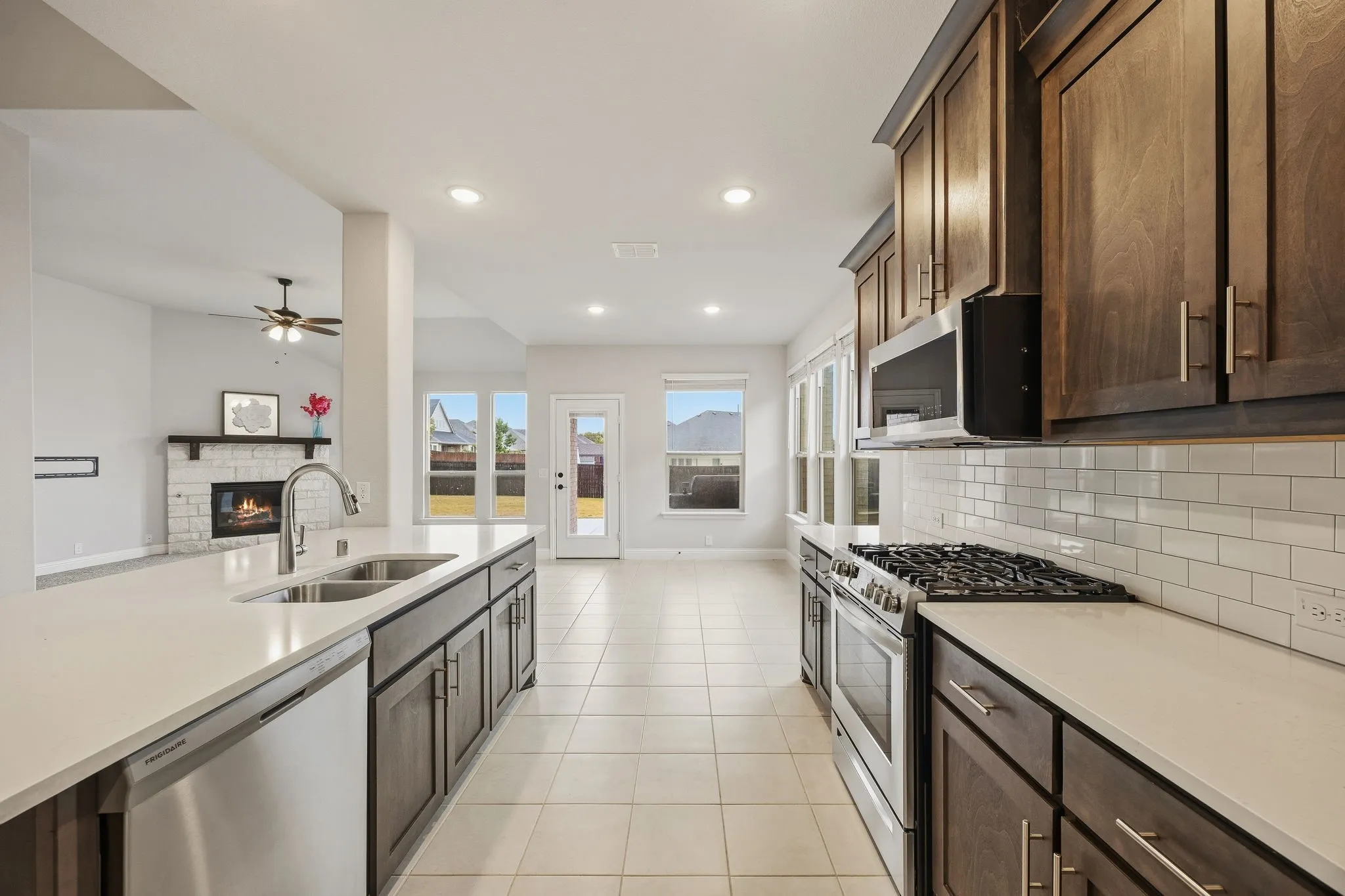 Kitchen featuring a double basin sink, stainless steel appliances, wood-finish cabinetry, subway tile backsplash, and light countertops