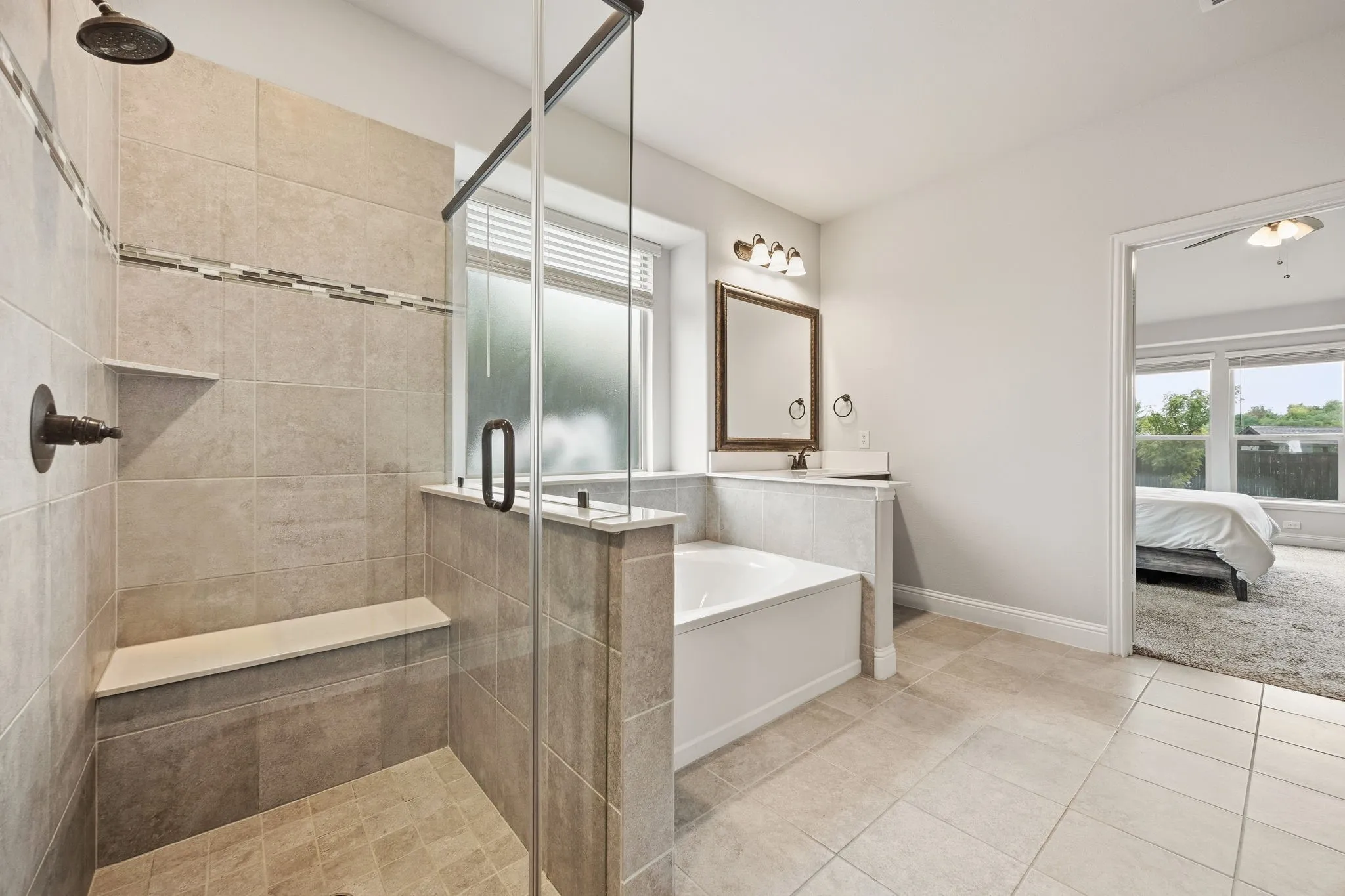 Tiled shower with built-in bench and glass enclosure, separate soaking tub, and tile flooring