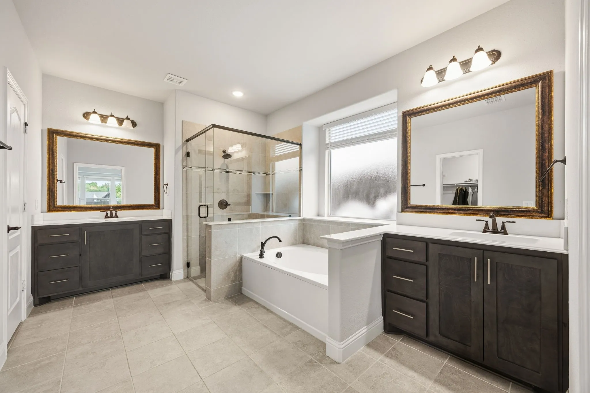 Dual vanity with undermount sinks, separate soaking tub, and enclosed glass shower with tile surround