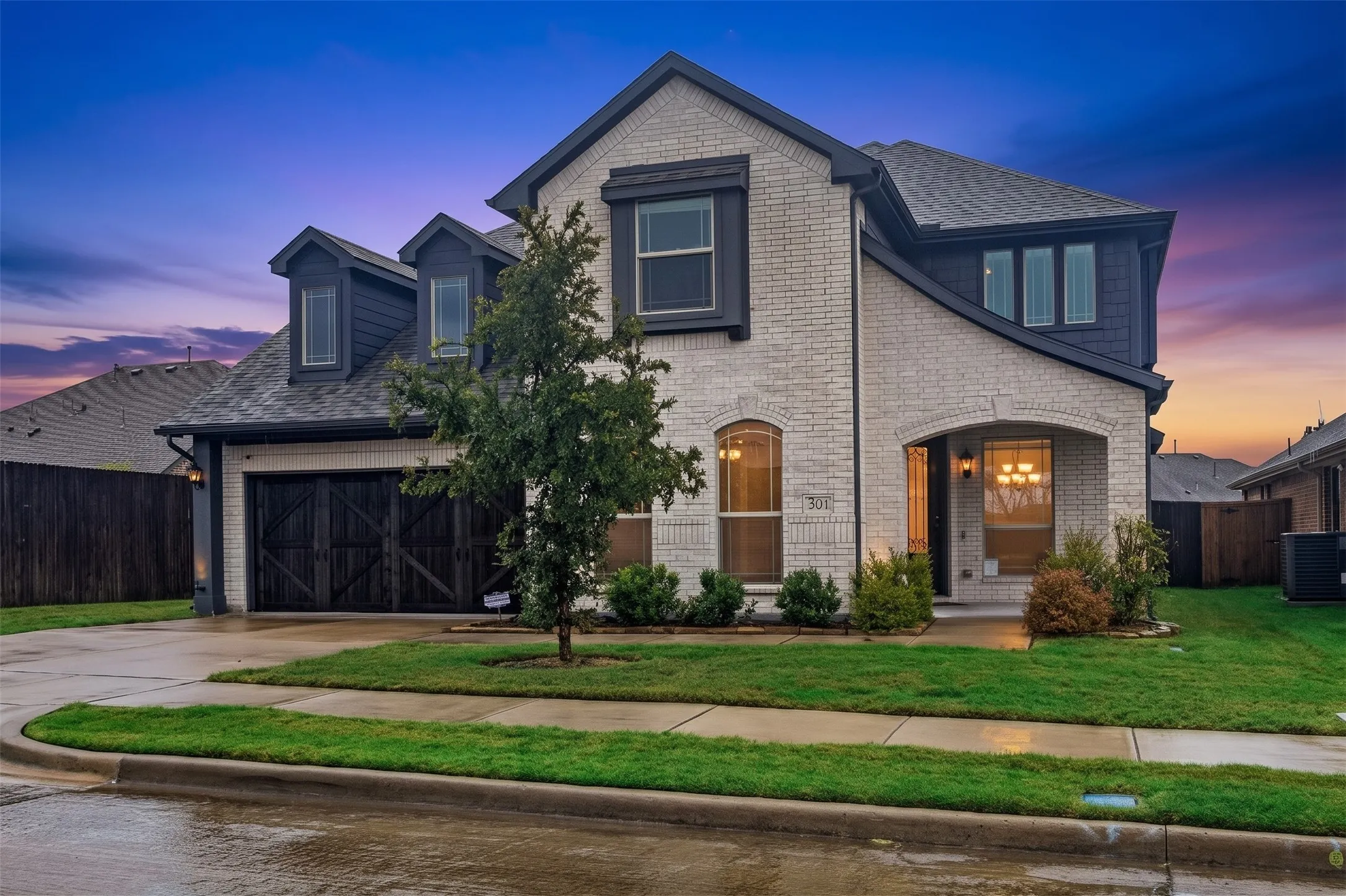 Brick and siding exterior with dark trim accents, covered entry, arched window, and a two-car garage with carriage-style doors