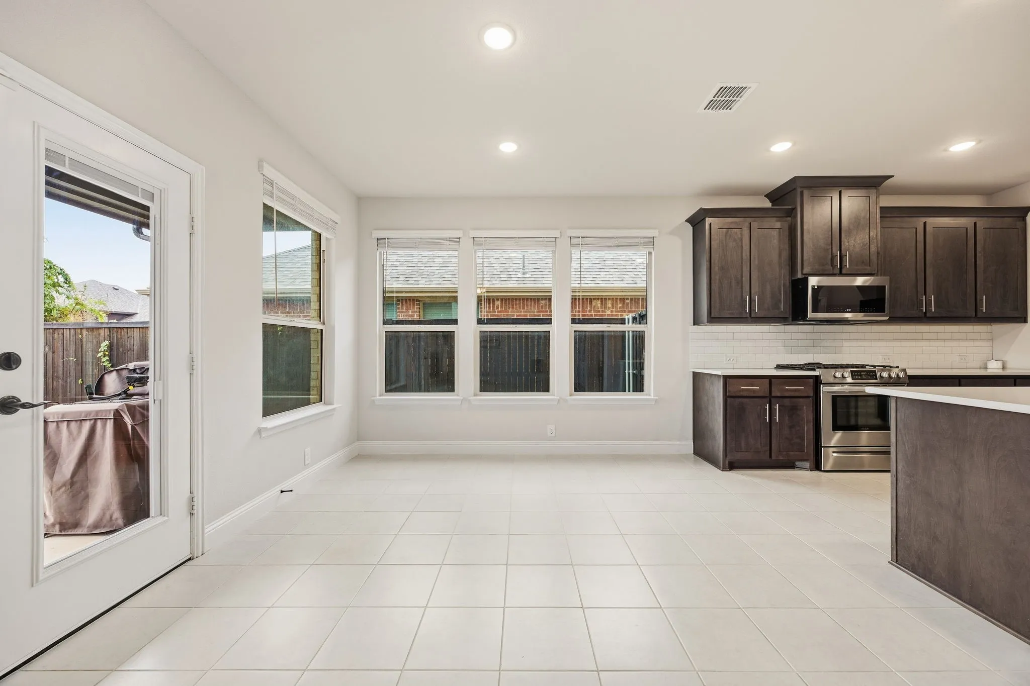 Spacious kitchen and dining area featuring ceramic tile flooring, recessed lighting, dark wood cabinetry, a subway tile backsplash, and stainless steel appliances