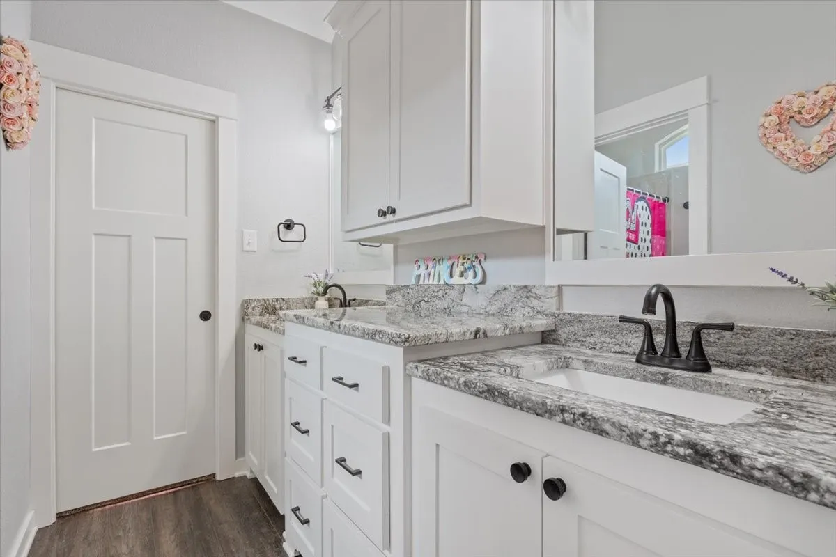 Dual vanity with under-mount sinks, speckled countertops, white cabinetry, and matte black hardware