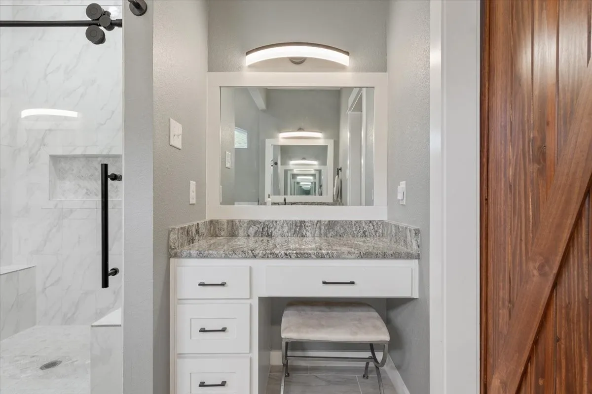 Built-in vanity with a stone-finish countertop, white cabinetry, and matte black hardware