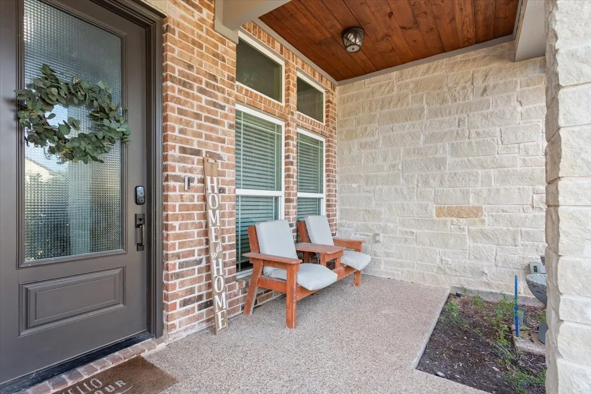 Brick and stone exterior with a textured glass front door, covered porch, and wood-paneled ceiling