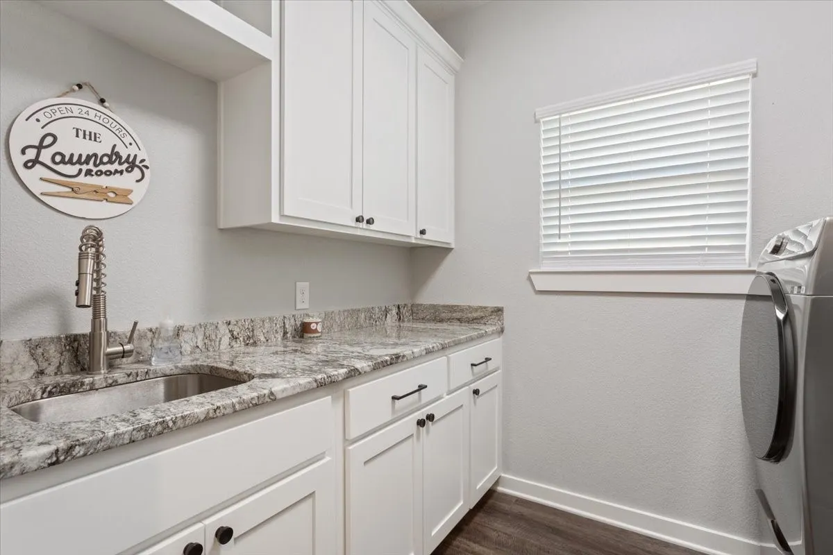 White cabinetry with matte black hardware, integrated sink with a pull-down faucet, stone-finish countertop, and wood-finish flooring