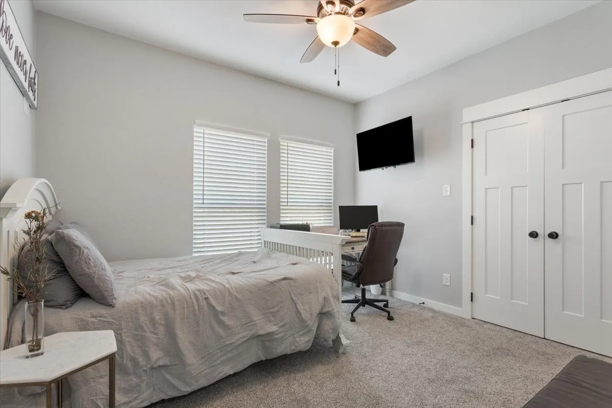 Ceiling fan with integrated lighting, dual windows with blinds, built-in closet with panel doors and dark hardware, wall-mounted television, and carpeted flooring