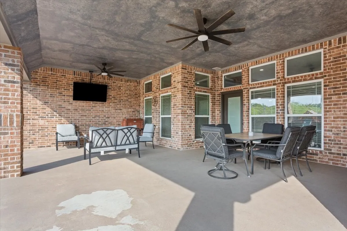 Covered outdoor living space featuring brick walls, concrete flooring, and multiple ceiling fans