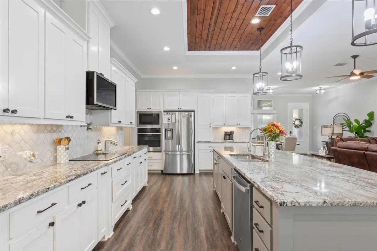 Expansive kitchen featuring white cabinetry, light-toned countertops, stainless steel appliances, wood-finish flooring, and a coffered wood ceiling detail
