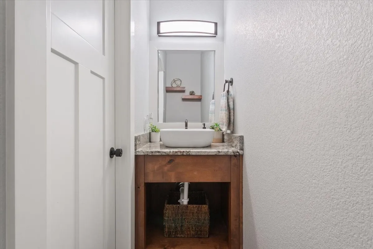 Vessel sink with a granite-style countertop, wood-finish vanity, and overhead vanity light fixture