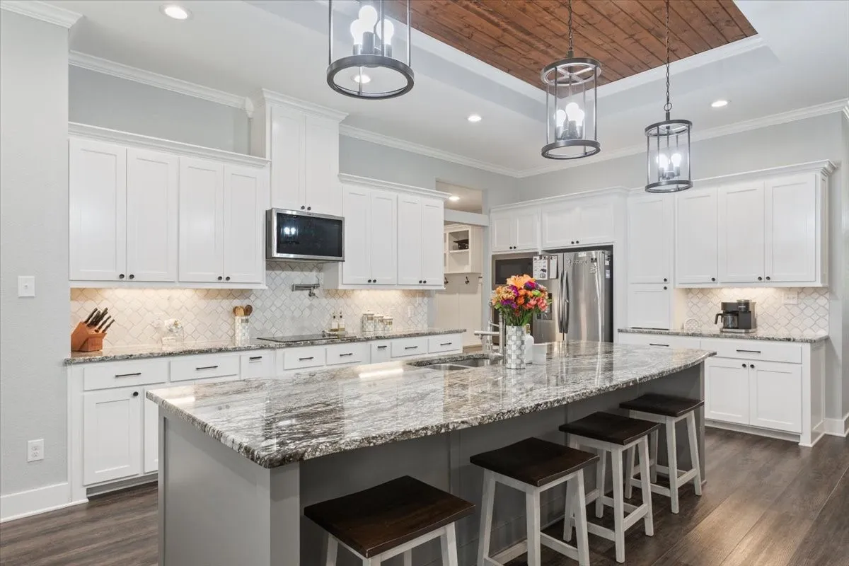 Spacious kitchen featuring white cabinetry, a large center island with a stone countertop, a tile backsplash, and wood-finish flooring