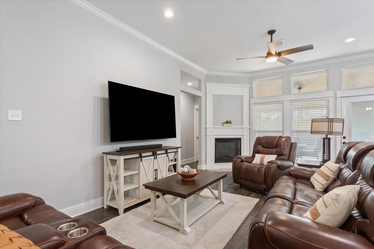 Recessed lighting, crown molding, wood-finish flooring, ceiling fan, and corner fireplace with mantel