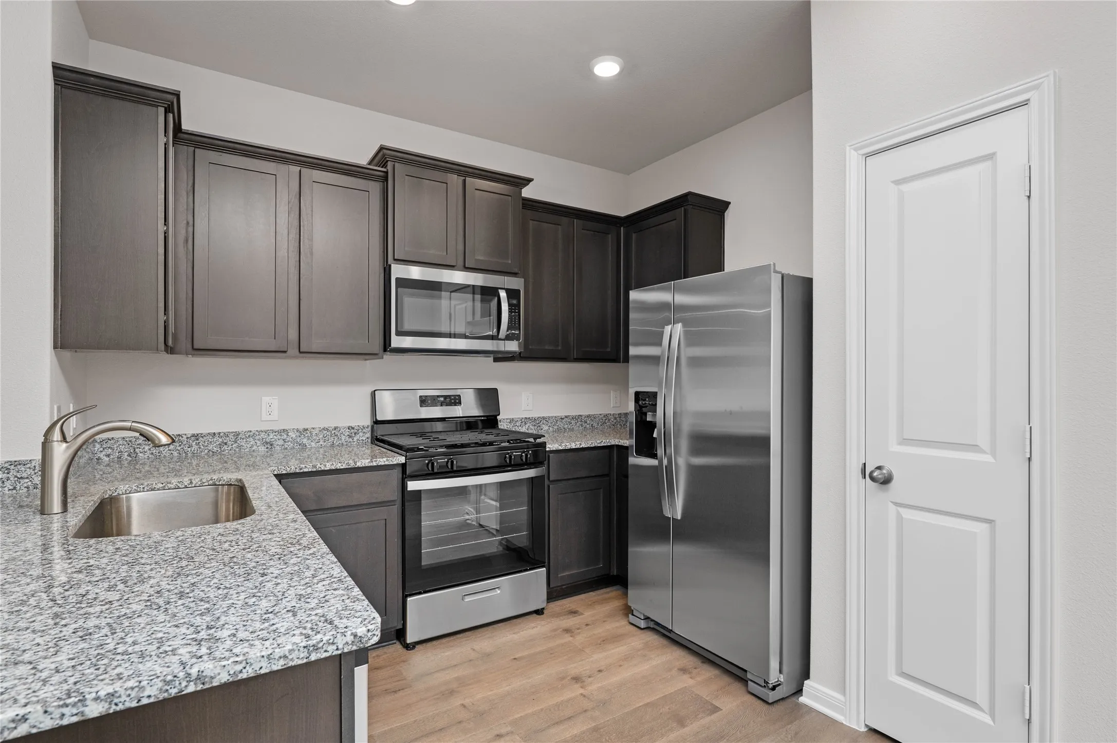 Kitchen featuring appliances with stainless steel finishes, light stone countertops, light wood-style flooring, and dark brown cabinets