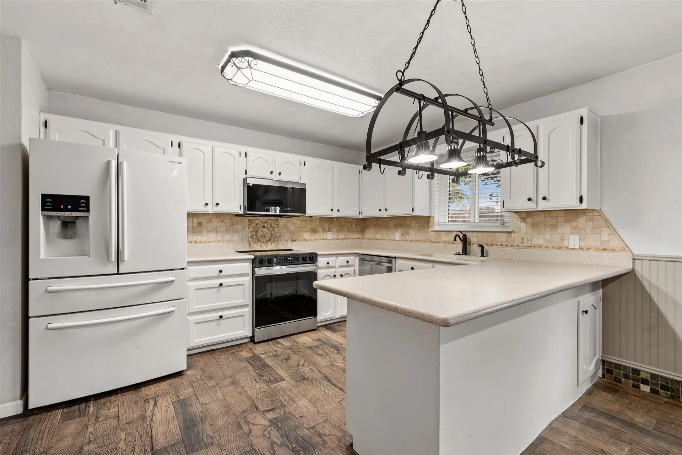 Kitchen featuring white cabinetry, wood-finish flooring, an island with countertop, stainless steel appliances, and a decorative pot rack fixture