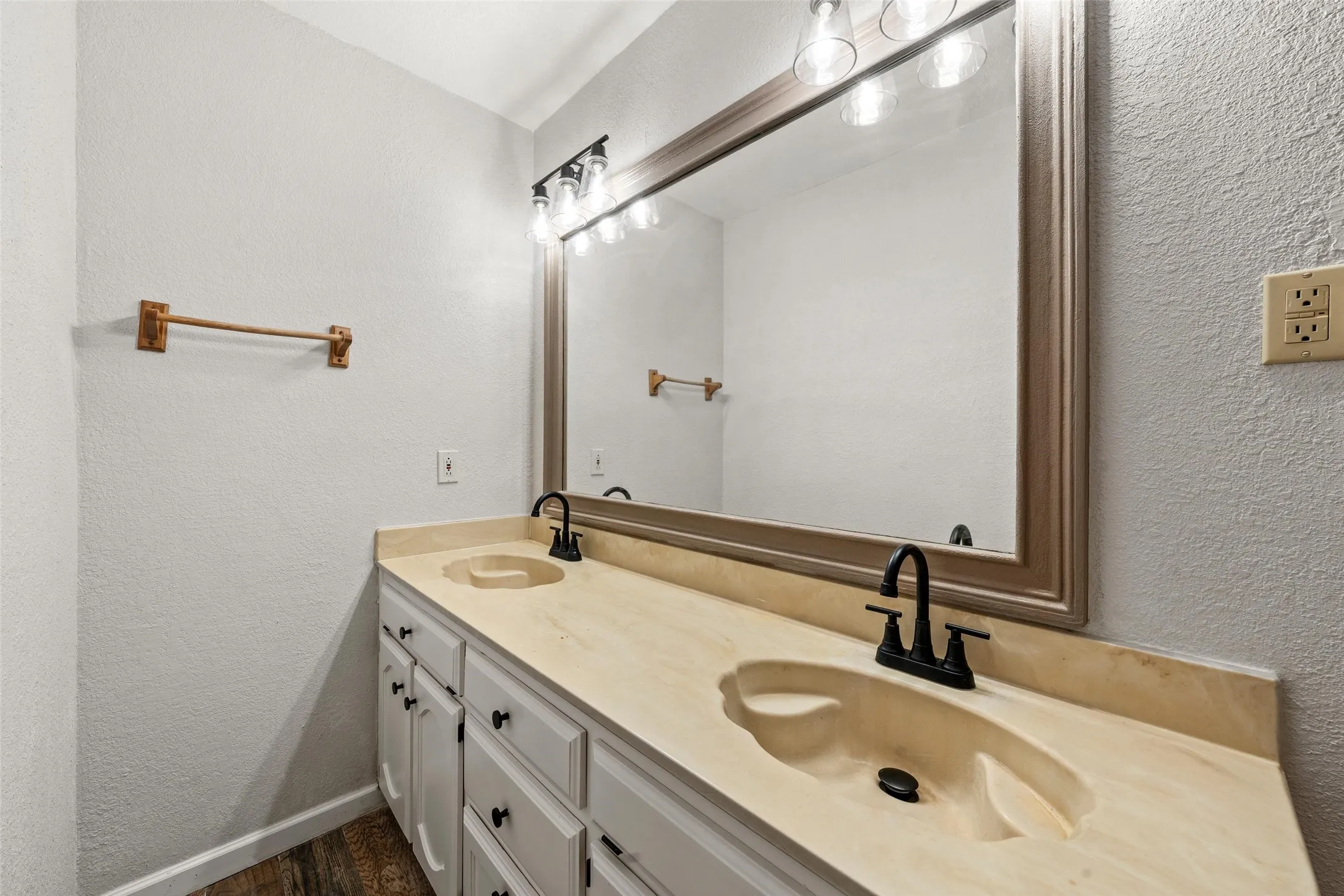 Double vanity with integrated sinks, matte black faucets, white cabinetry, and wood-finish flooring