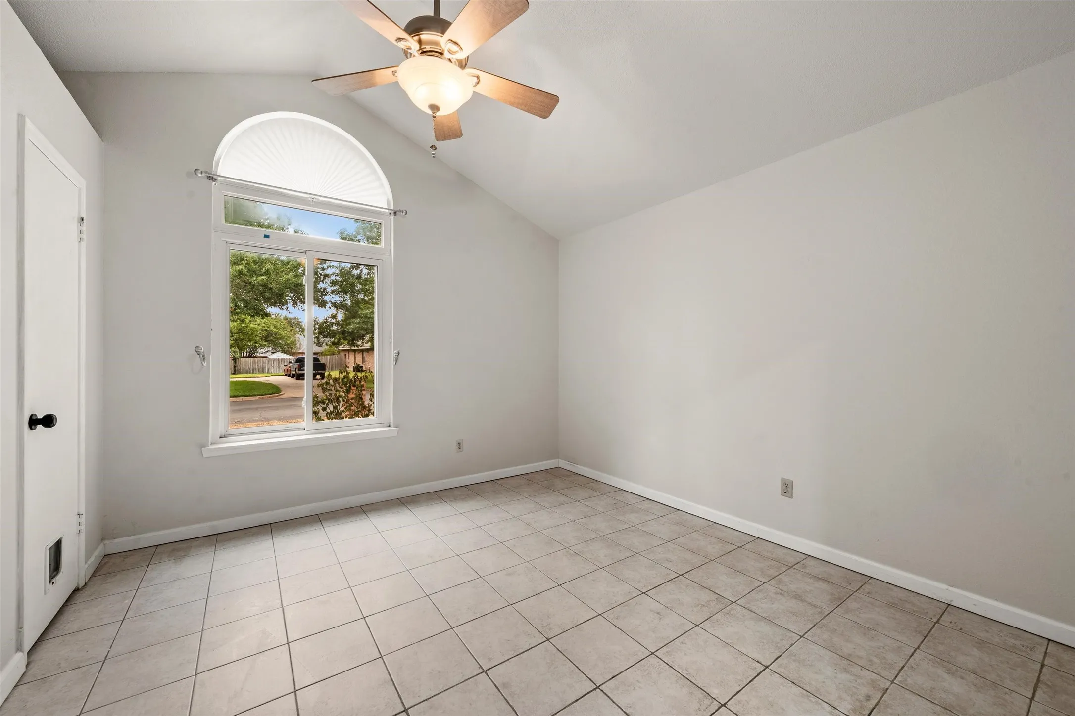 Vaulted ceiling with an attached ceiling fan and light fixture, large arched window, tiled flooring, and a white paneled door