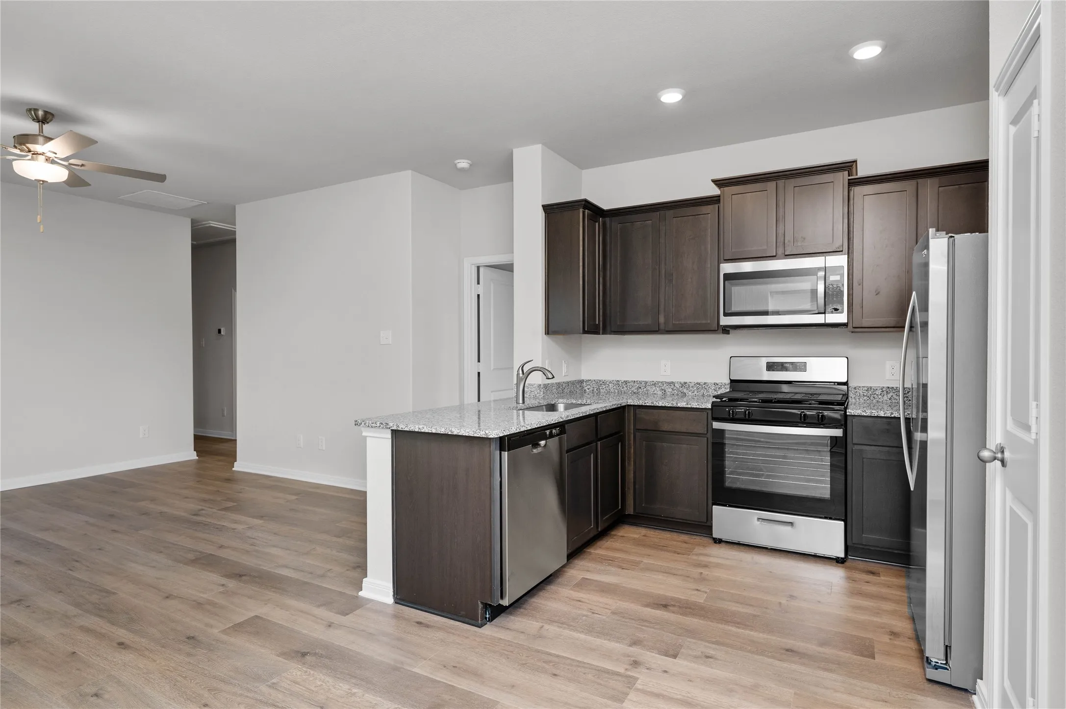 Kitchen with appliances with stainless steel finishes, dark brown cabinets, a peninsula, light wood-style floors, and light stone counters